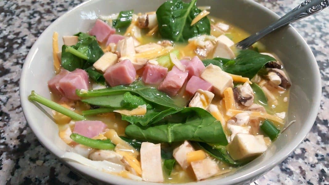 eggs, milk, salt, ham, spinach, mushrooms, cheese, and green onion mixed in a bowl with a spoon for baked omelets