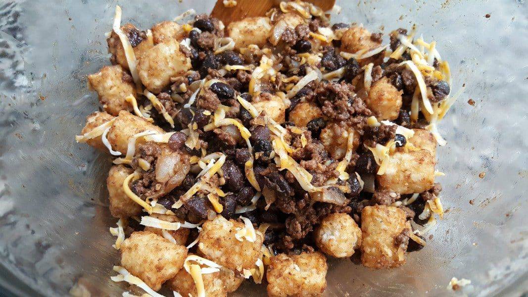 ground beef, black beans, tater tot, and colby jack cheese mixed in a bowl