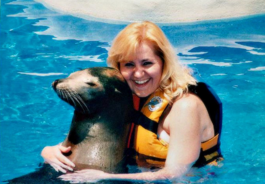 a woman wearing a life jacket hugging a sea lion in water