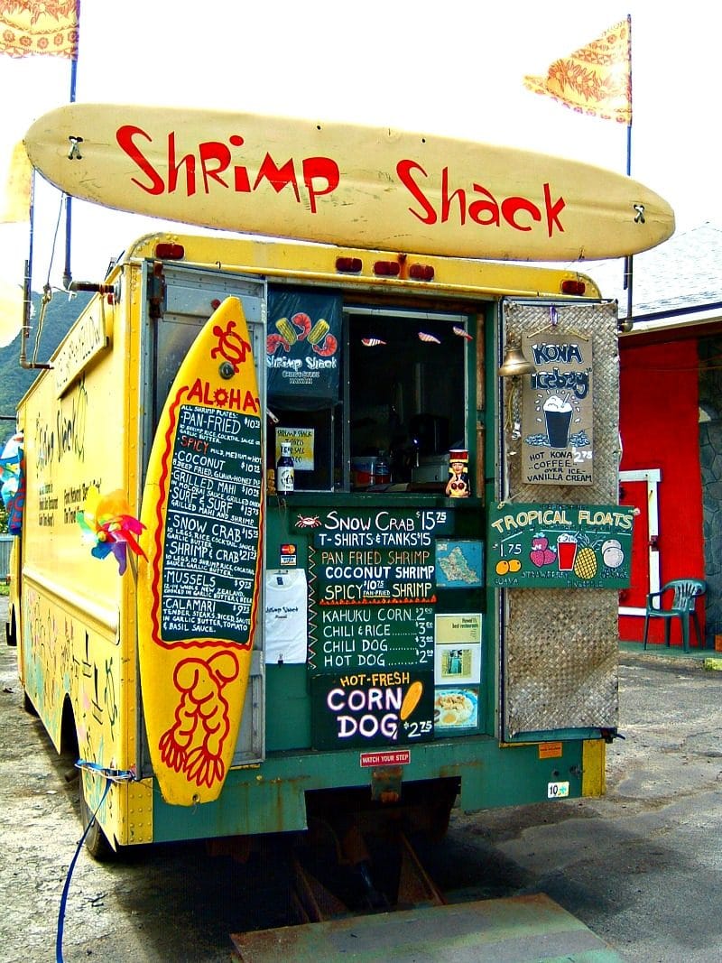 a view of a food truck called The Shrimp Shack with a large surf board as the menu and the order window on the back of the truck