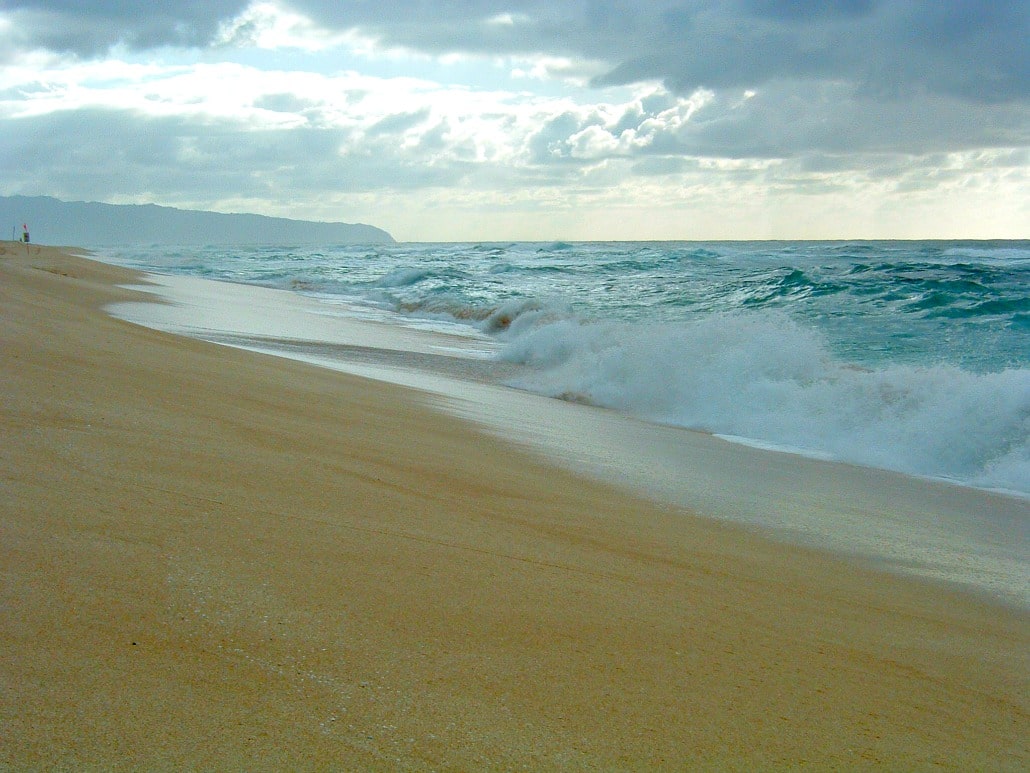 a sandy beach with waves crashing on the shore and a mountain in the distance