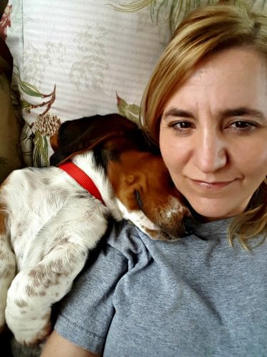 blond woman cuddling with a basset hound puppy on a sofa