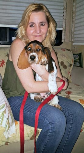 a blond woman holding a basset hound puppy sitting on a chair