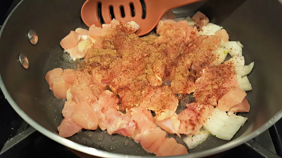 cooking chicken, onion, and spices in a frying pan
