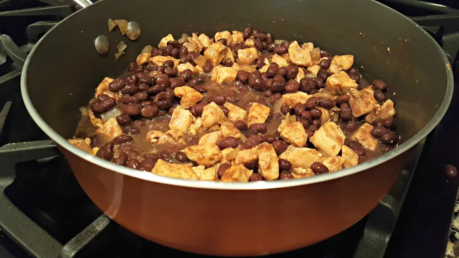 adding black beans to sauted chicken in frying pan