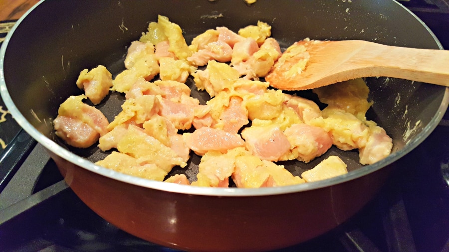 chicken coated in egg mixture frying in a pan with wooden spoon