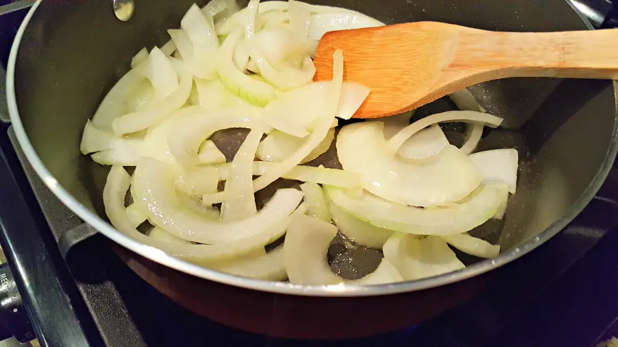 onions cooking in a pan with a wooden spoon.