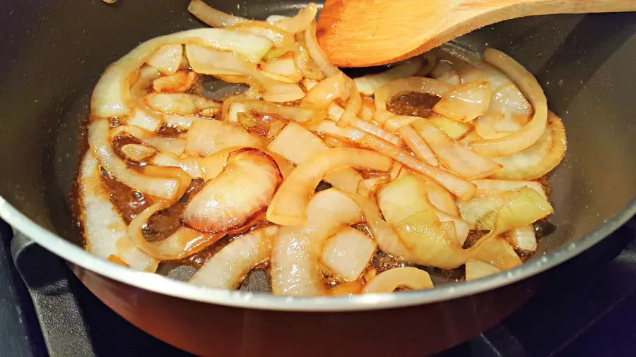 caramelized onions cooking in a pan with a wooden spoon.