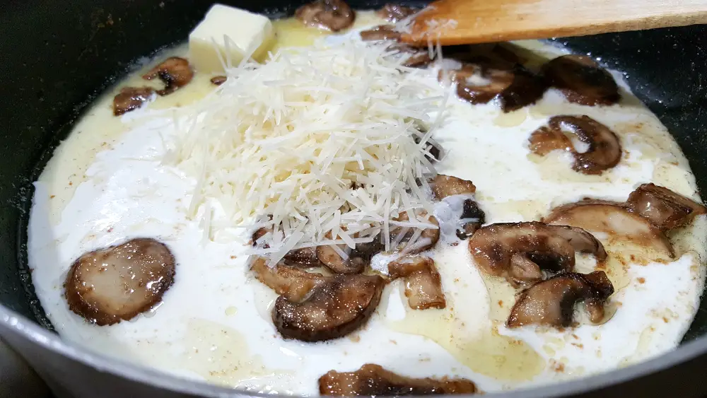 mushrooms, butter, heavy cream, and Parmesan cooking in a frying pan.