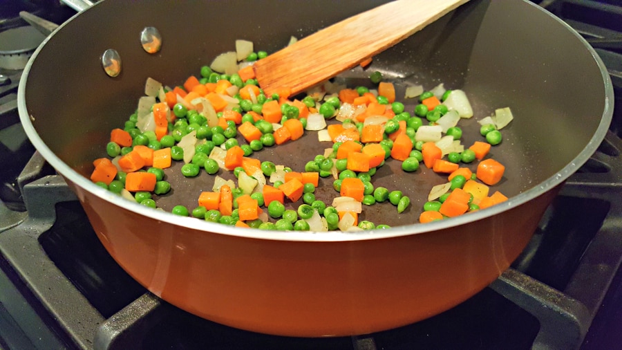 peas, carrots and onions cooking in a pan.