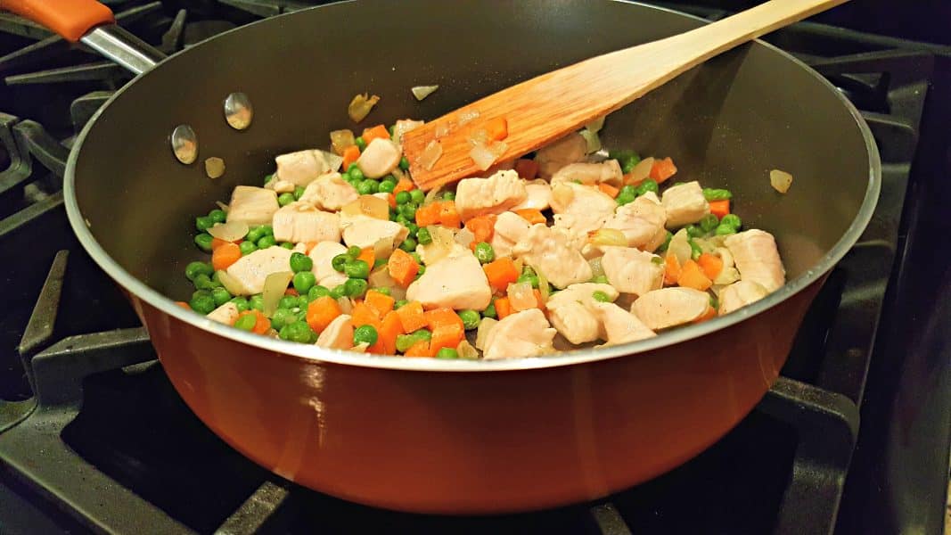 chicken, peas, carrots and onions cooking in a pan.
