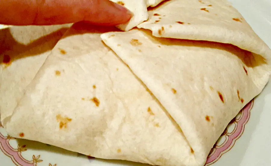 a finger folding the tortilla crunchwrap edges in toward the center