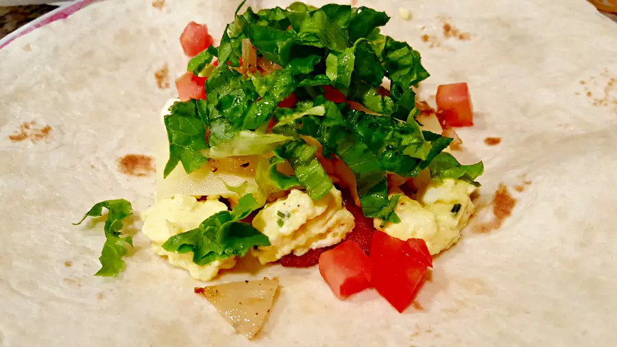 bacon, egg, cheese, onion, tomato, and lettuce on a tortilla