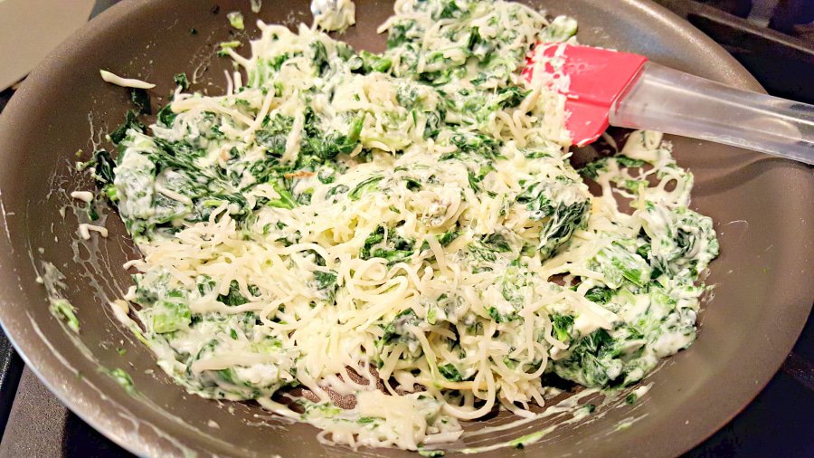 cooking spinach, cream cheese, and Italian cheese in a pan