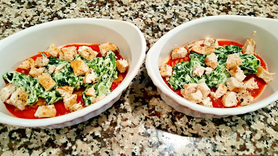 two baking dishes with chicken on top of spinach mixture