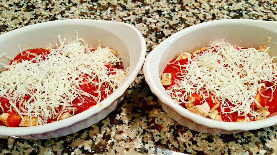 two baking dishes with chicken, sauce and cheese