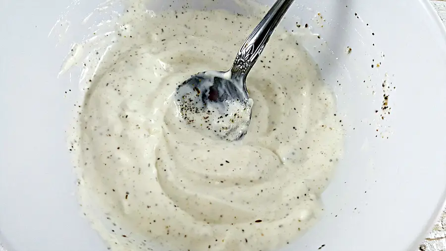 mayo, sour cream, vinegar, garlic powder, salt and pepper mixed in a bowl with a spoon.