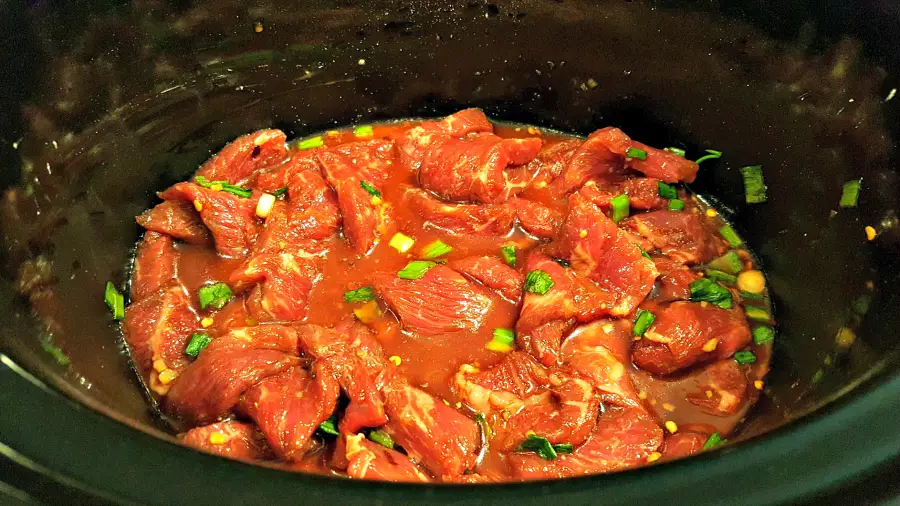 Mongolian beef, sauce, and green onions in a slow cooker crock pot