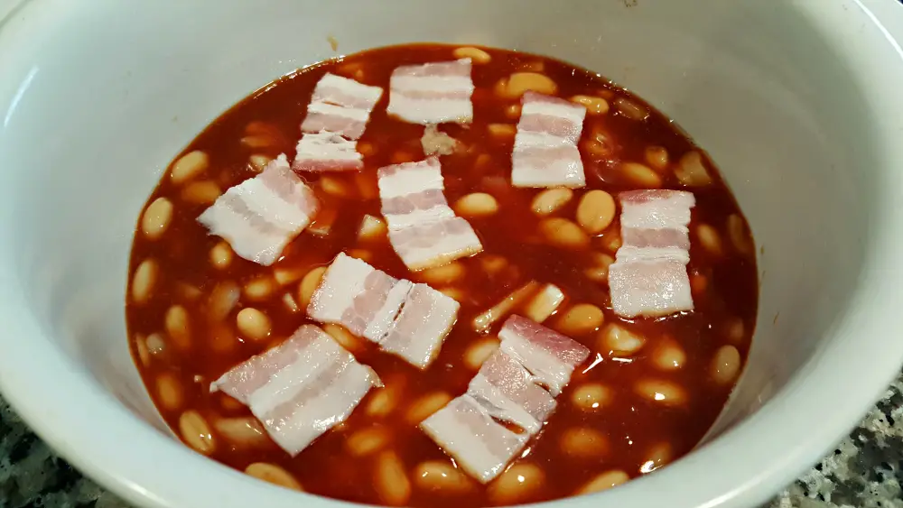 bacon pieces layered on top of beans ingredients ready to bake.