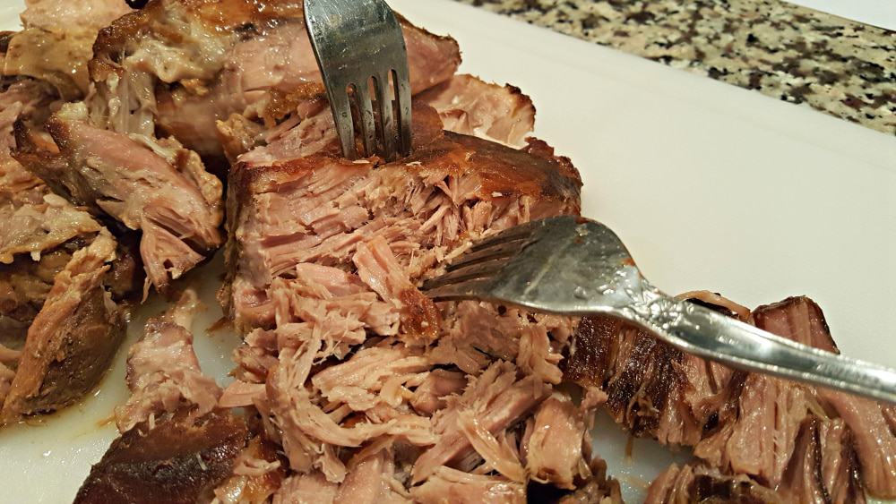 two forks shred pork roast apart on a cutting board