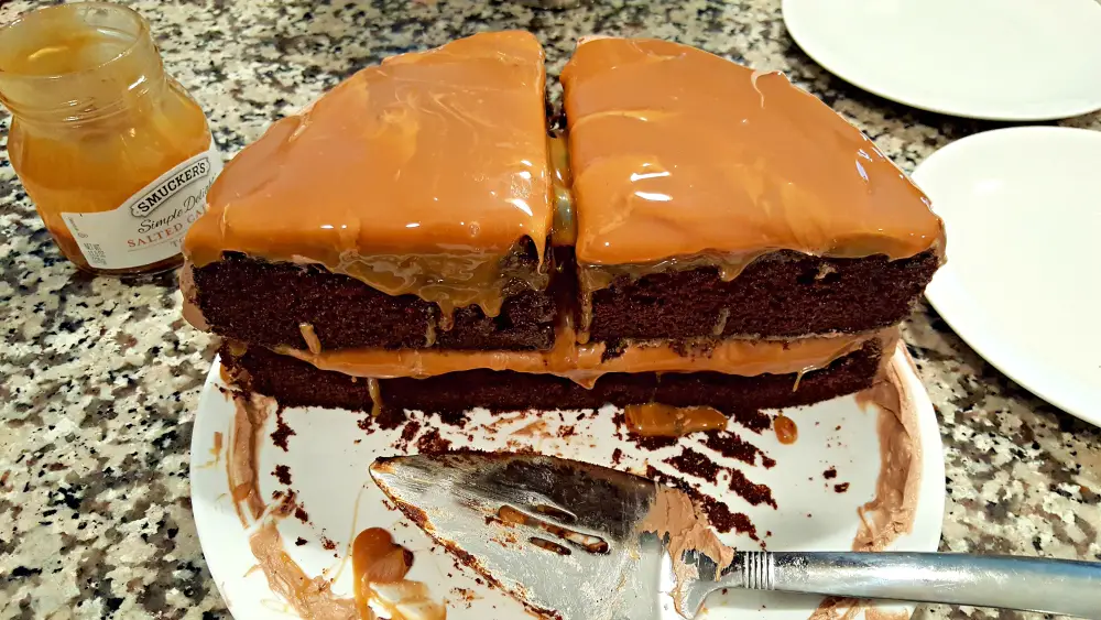 two pieces of two layer chocolate cake with salted caramel topping on a plate with a pie server