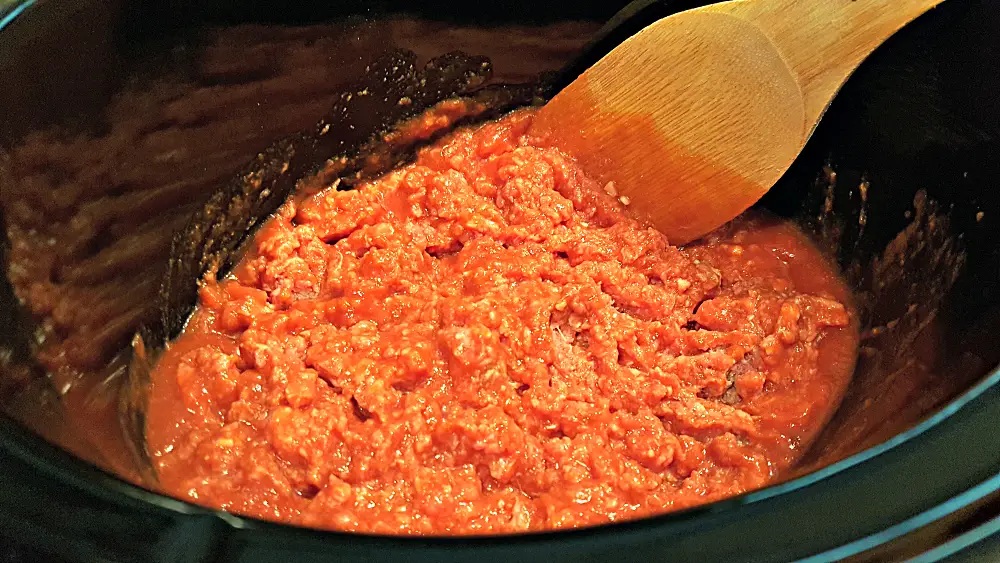 adding ground beef and tomato sauce to the slow cooker.