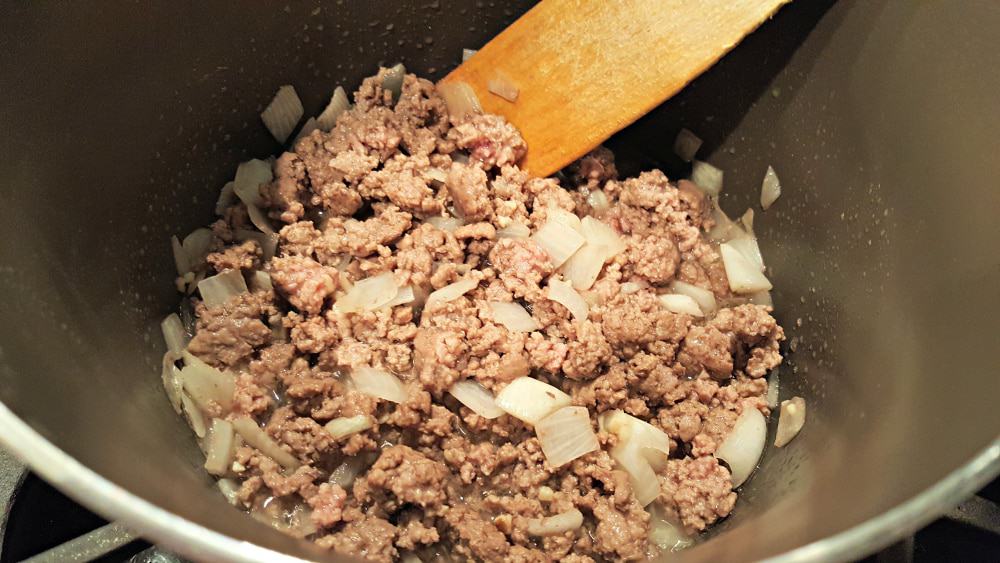 ground beef and onion cooking in a sauce pan with a wooden spoon.