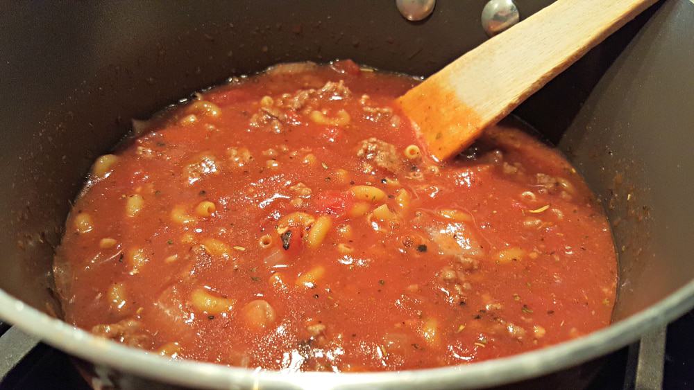 goulash cooking in a pan with a wooden spoon.