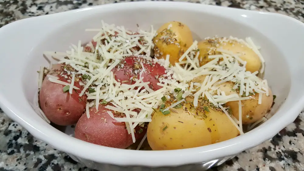 olive oil, garlic, thyme, oregano, basil, chives, onion flakes, and Parmesan sprinkled onto potatoes in a baking dish