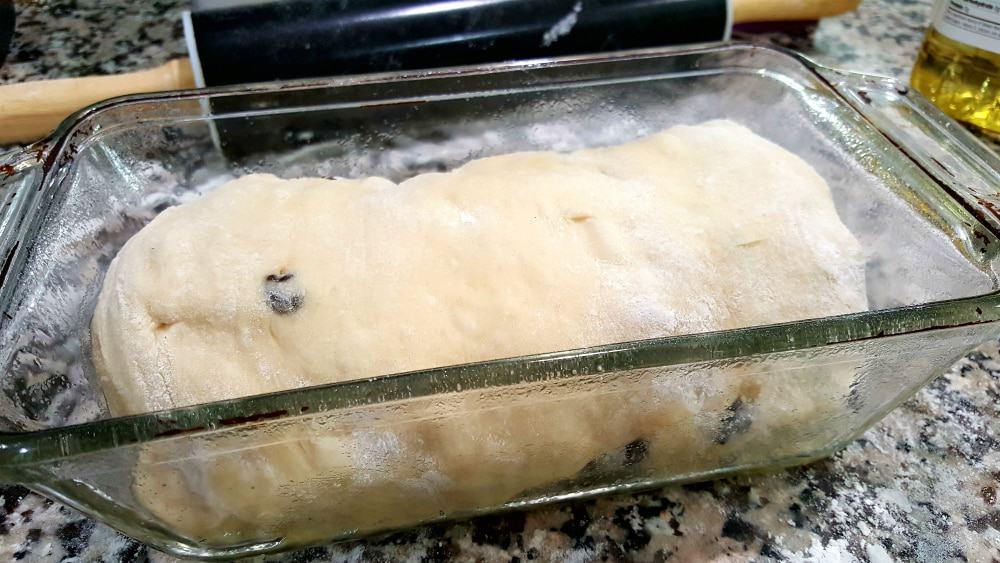 cinnamon raisin bread dough rolled into a roll inside a loaf pan.