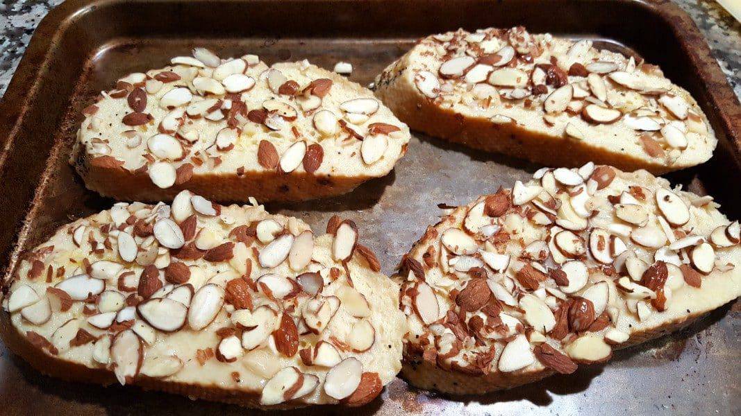 four slices of egg soaked bread topped with almonds on a baking sheet