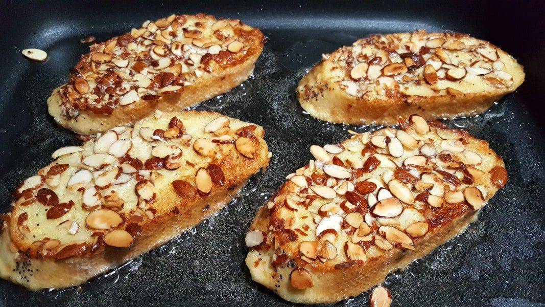 four slices of bread topped with almonds cooking in an electric skillet