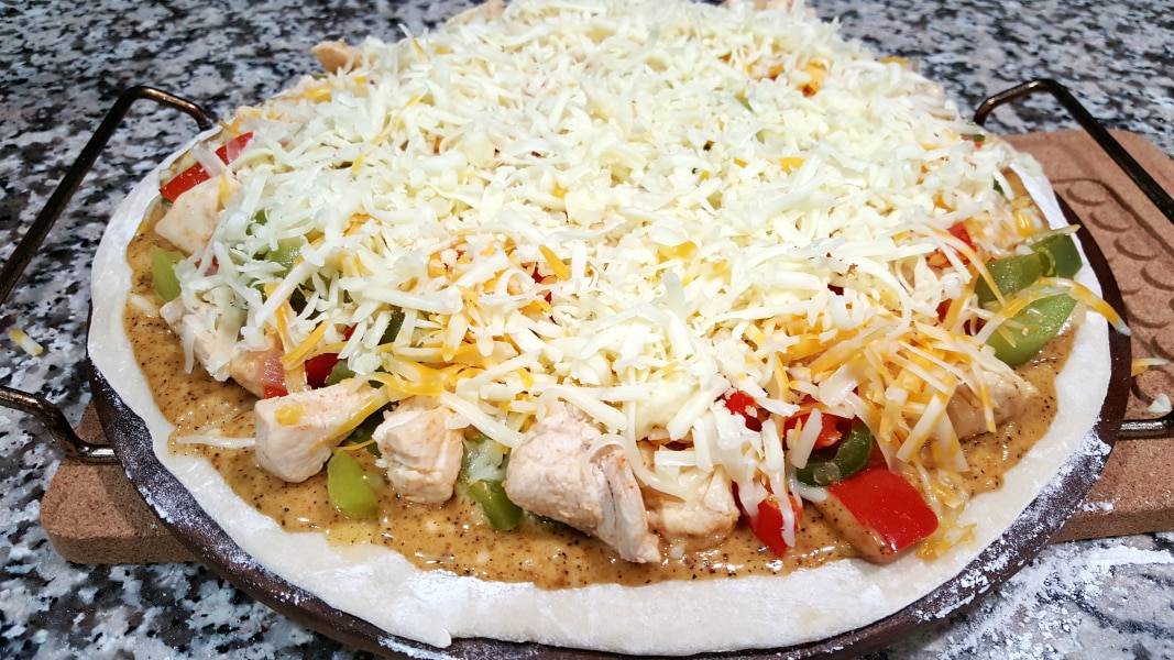 pizza dough topped with orange sauce, chicken, green pepper, red pepper, onions, and shredded cheese