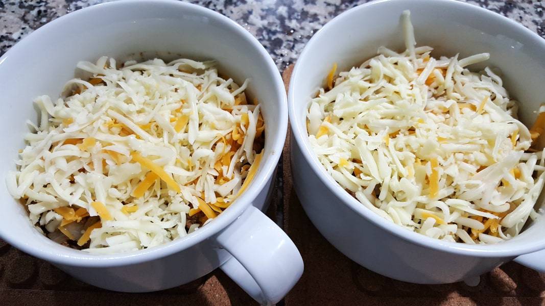 two round baking dishes with ground beef mixture topped with shredded cheese