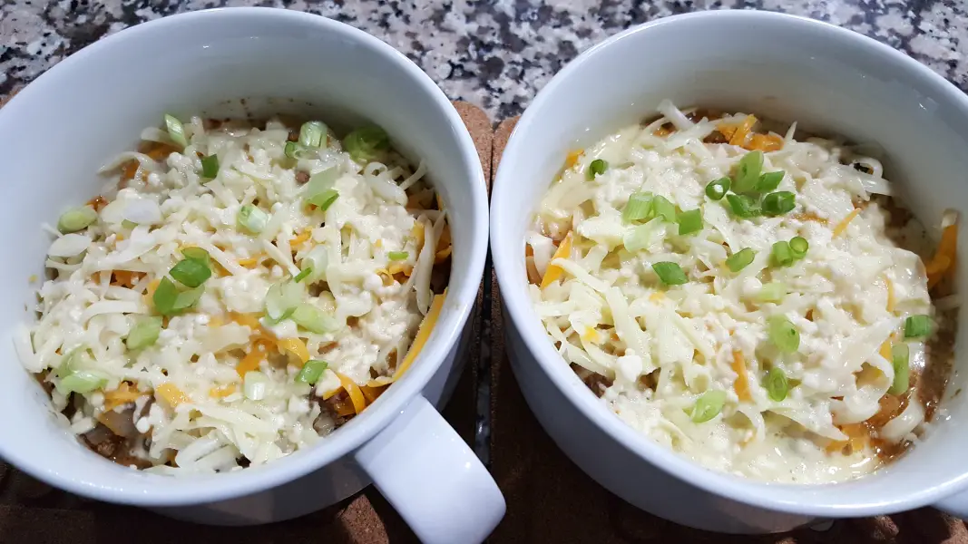 two round baking dishes, cheese is topped with diced green onions