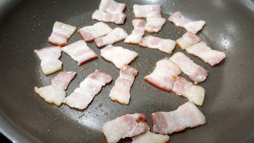 bacon pieces frying in a pan.
