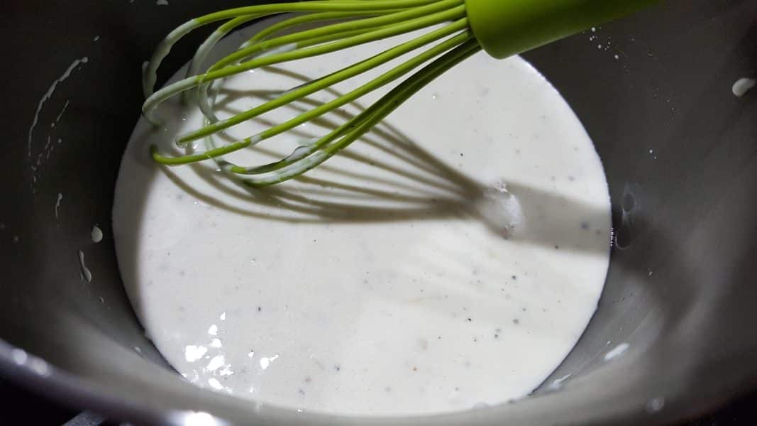 cheese sauce cooking in a pan with a whisk