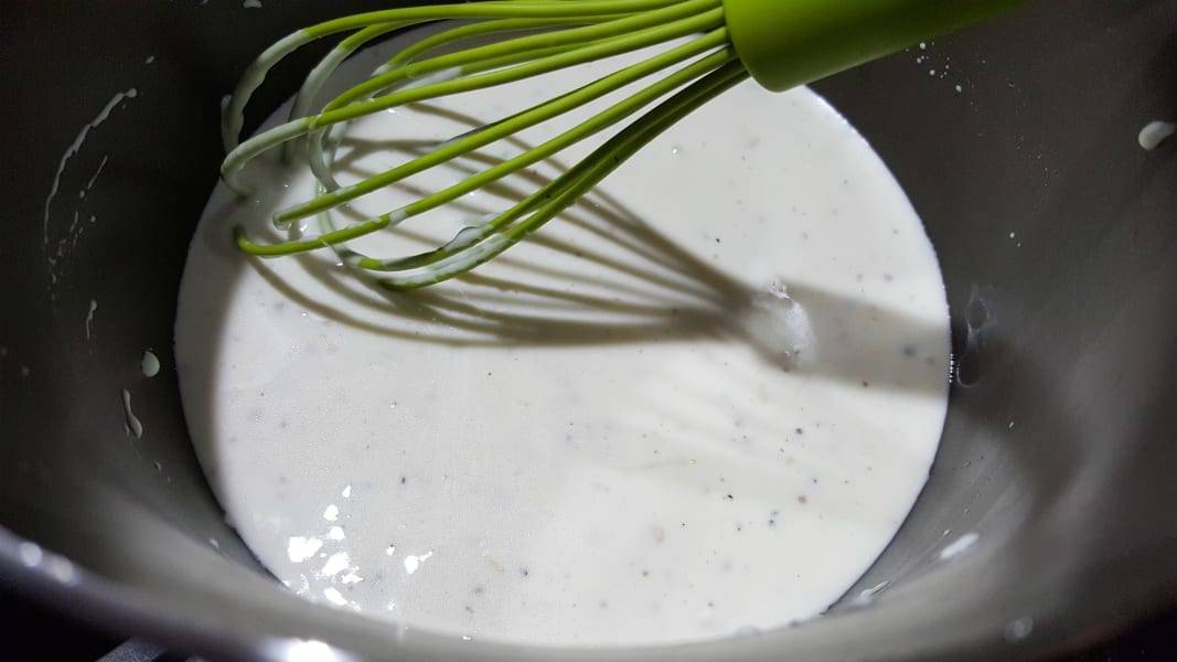 cheese sauce cooking in a pan with a whisk.