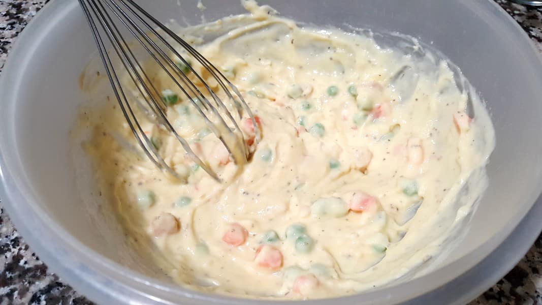 frozen peas and carrots, milk, cream of chicken soup, salt, pepper, dried minced onions, melted butter, garlic powder, and Italian seasoning in a bowl with a whisk.