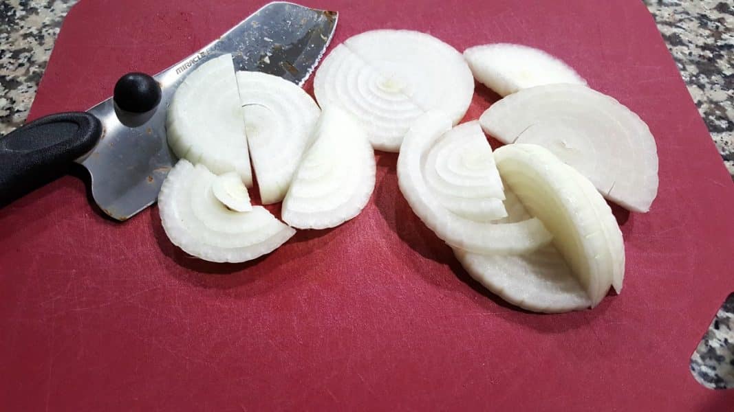 sliced onions, a chef knife, on a cutting board