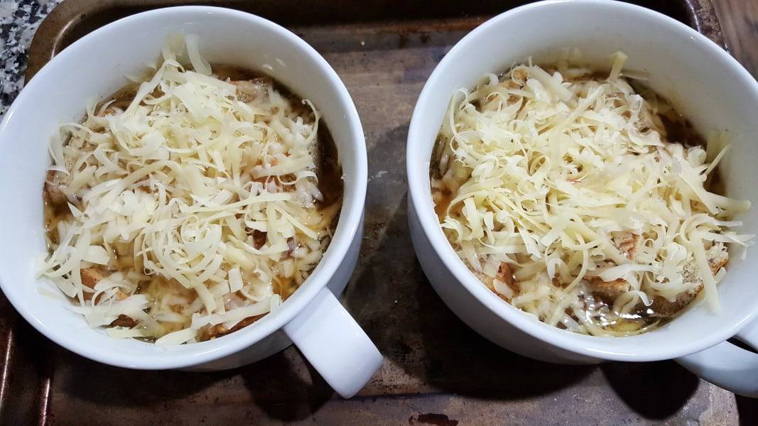 cheese sprinkled over American French Onion Soup and croutons in two soup bowls.
