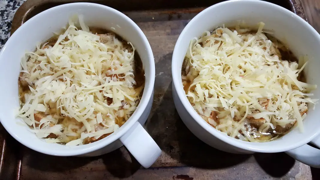 cheese sprinkled over American French Onion Soup and croutons in two soup bowls.
