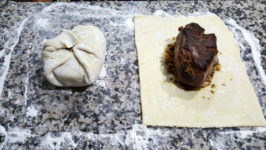 one beef wellington wrapped in puff pastry, one unwrapped on top of pastry.