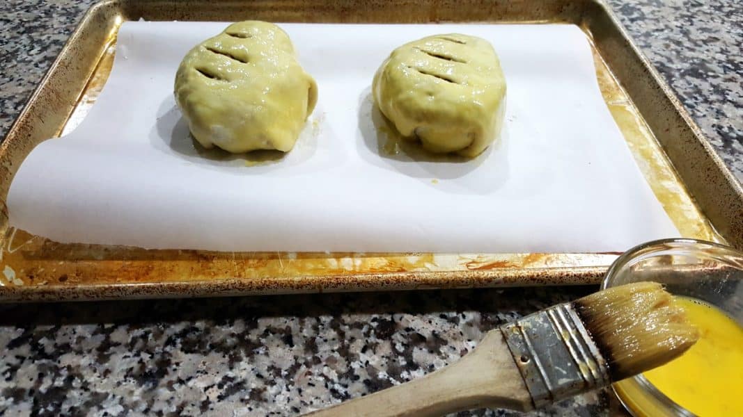two uncooked beef wellington parcels brushed with egg wash