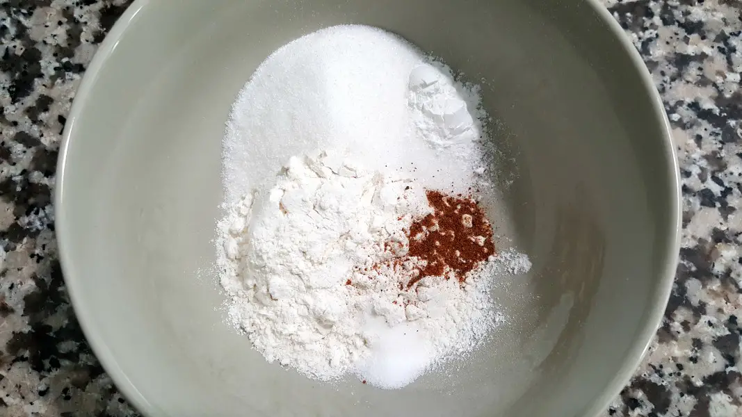 flour, sugar, baking powder, salt and nutmeg in a tan bowl.