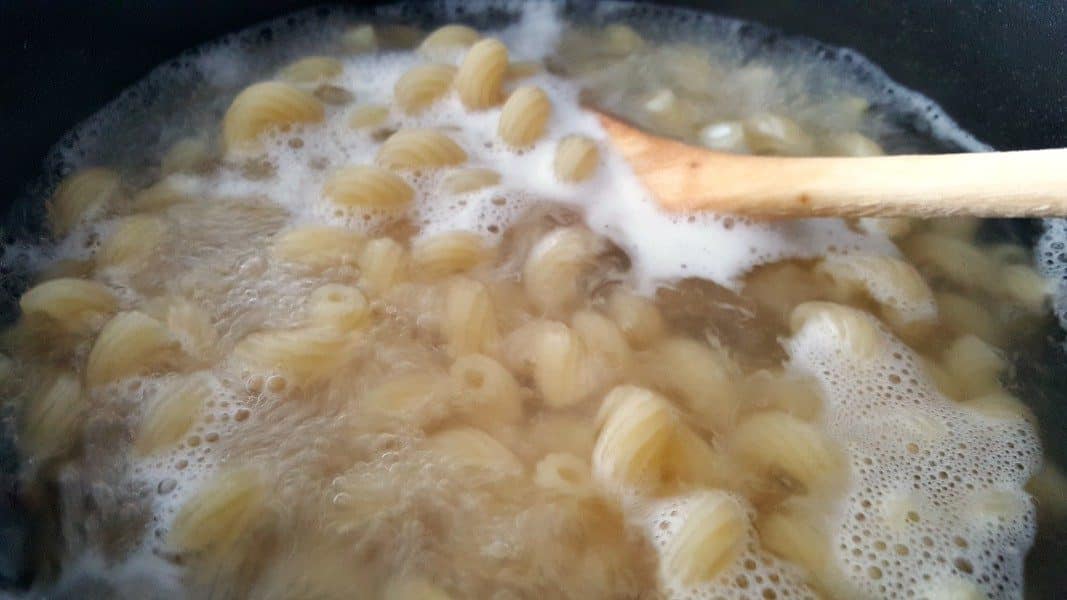 cavatappi pasta boiling in a ban with a wooden spoon