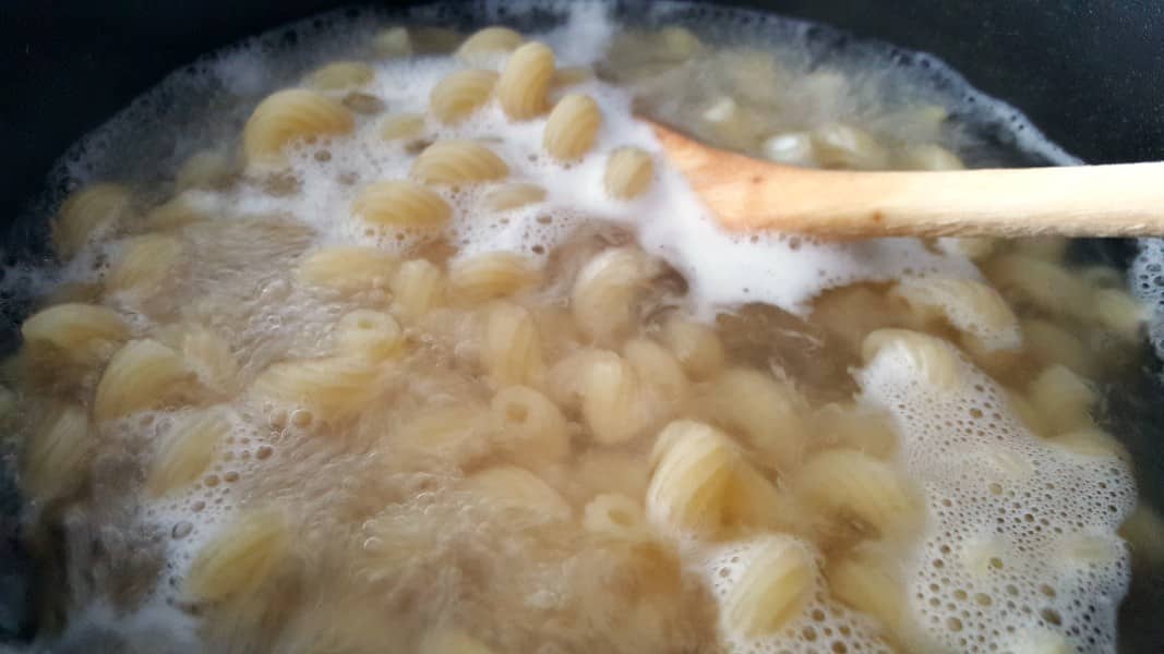 cavatappi pasta boiling in a ban with a wooden spoon.