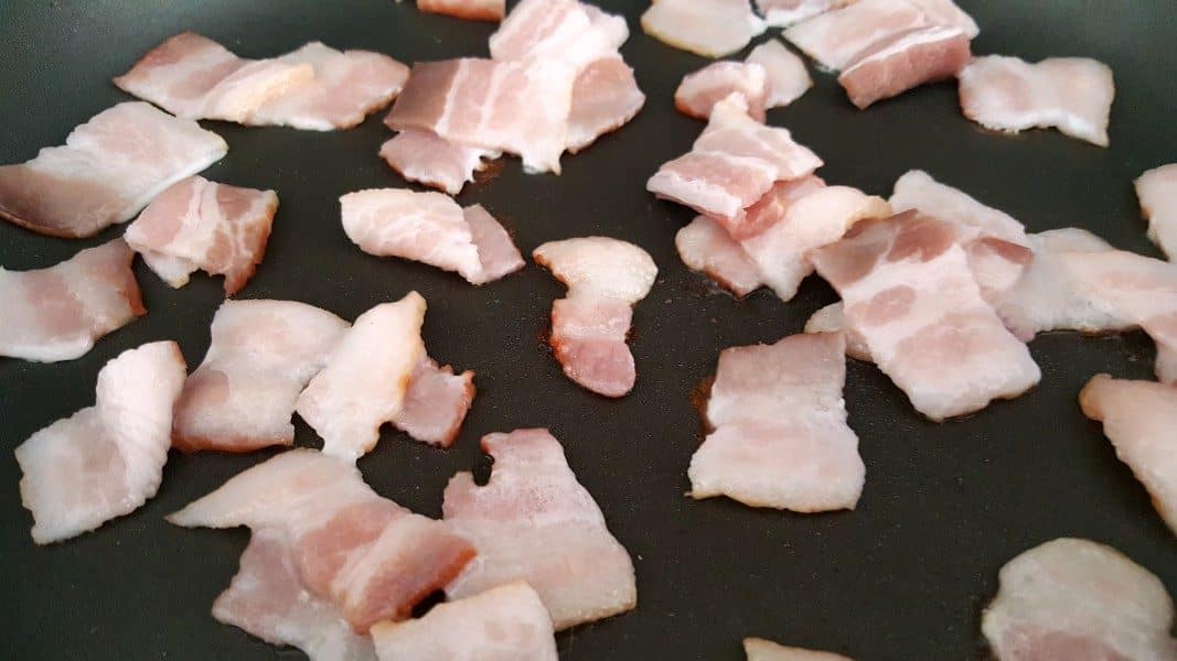 1 inch pieces of bacon frying in a pan