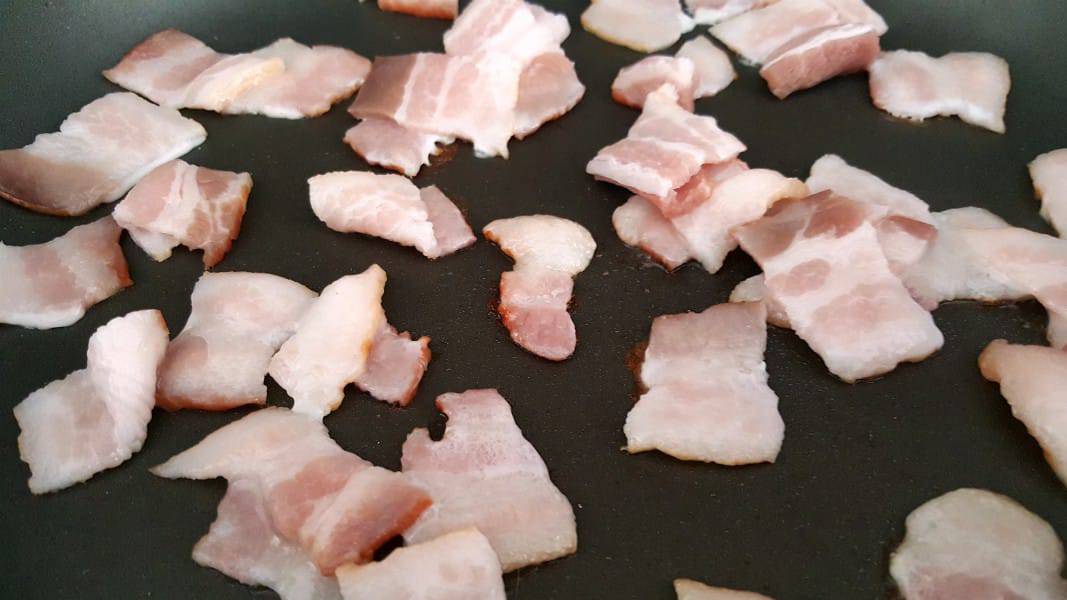 1 inch pieces of bacon frying in a pan.
