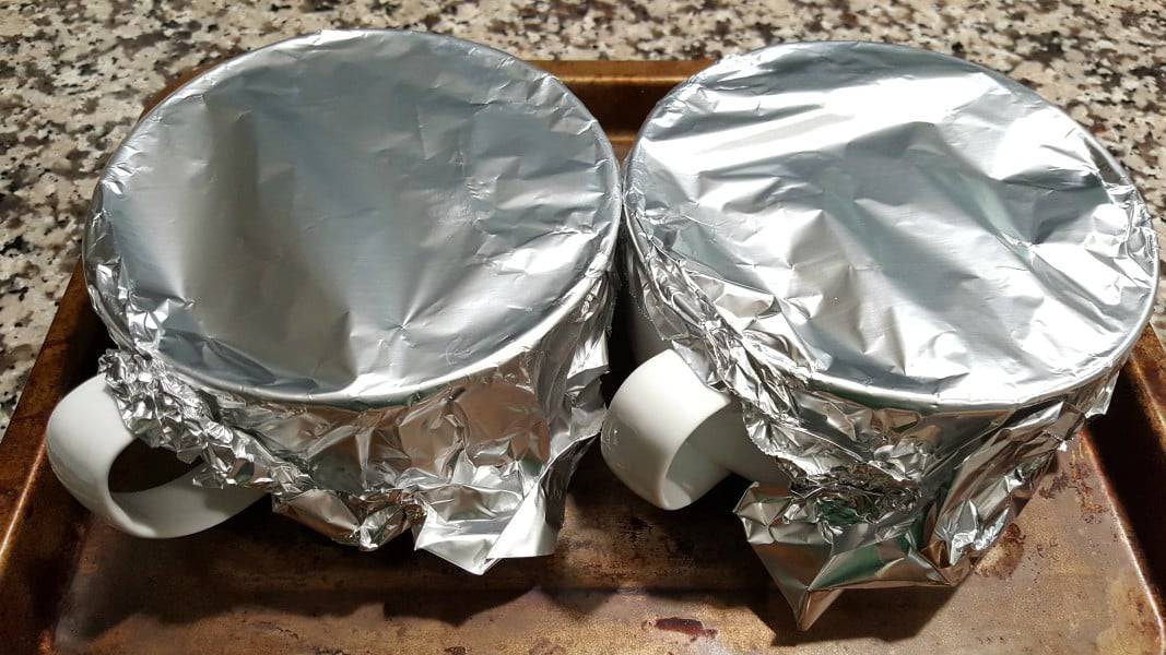 two bowls covered with foil on a baking sheet.